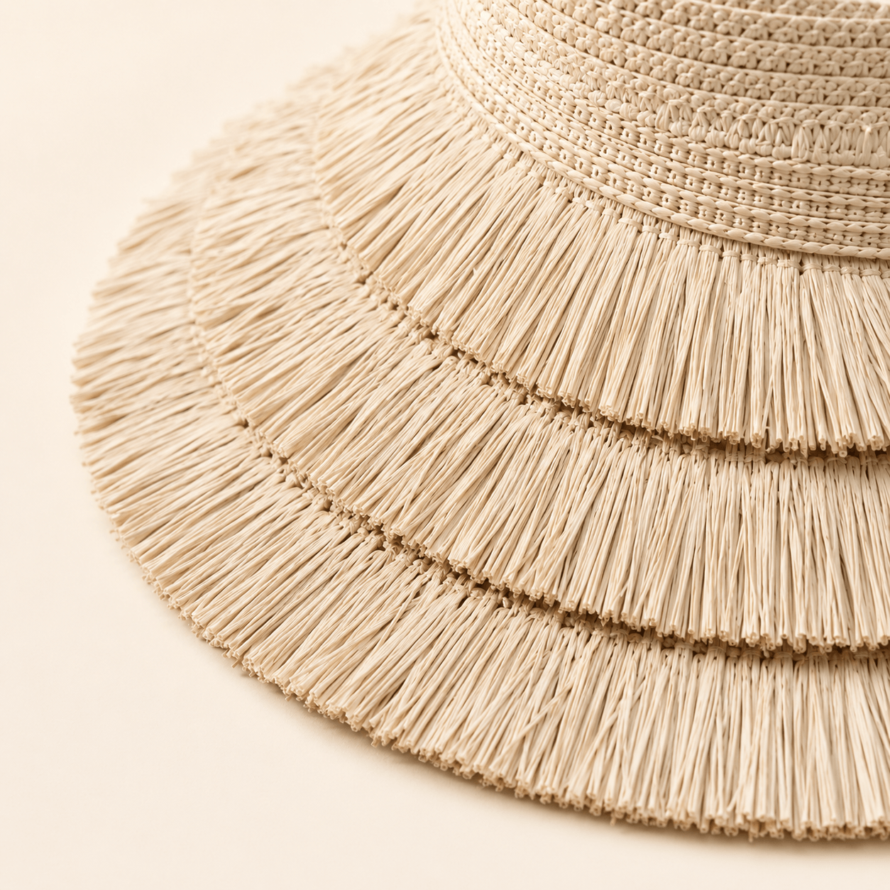 Close-up of the layered fringe brim detail on a beige woven straw visor hat