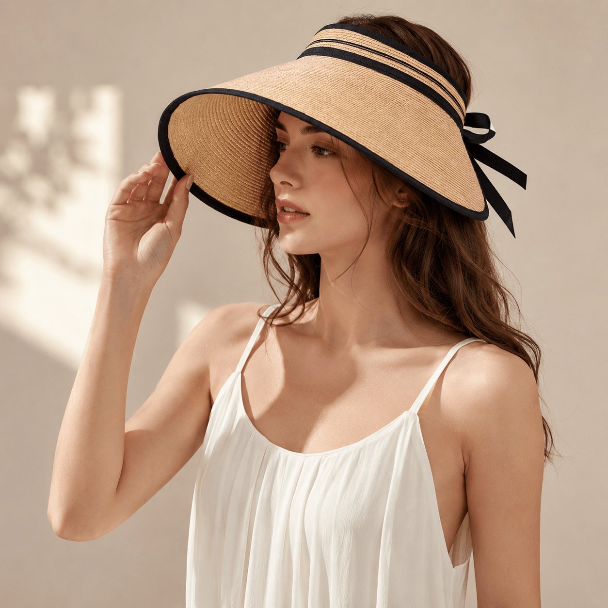 Woman wearing a light coffee wide brim paper straw visor hat with black trim and ribbon tie