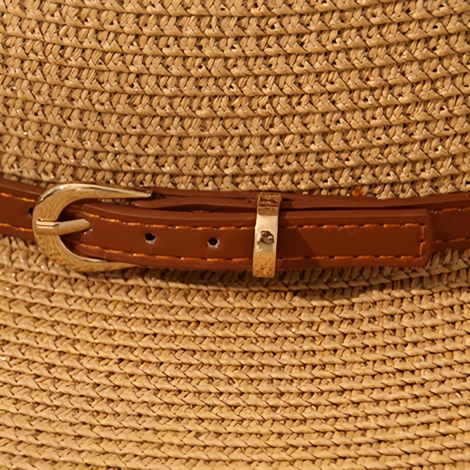 Close-up of brown leather hat band with gold buckle and fine stitching, highlighting craftsmanship.