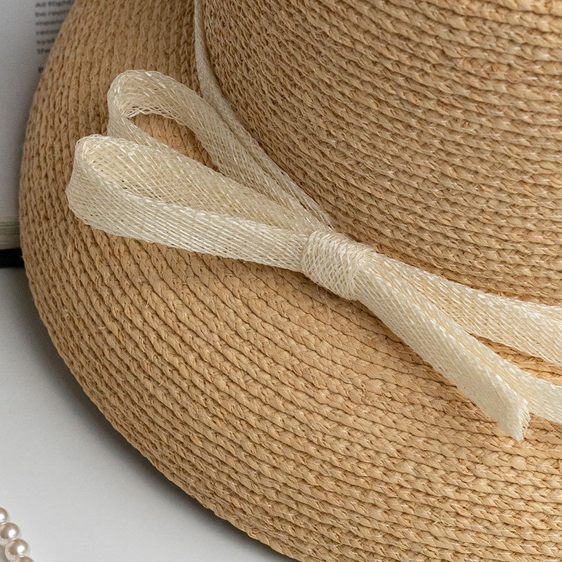 Close-up of woven straw hat bow, showing delicate ribbon weave and detailed craftsmanship.