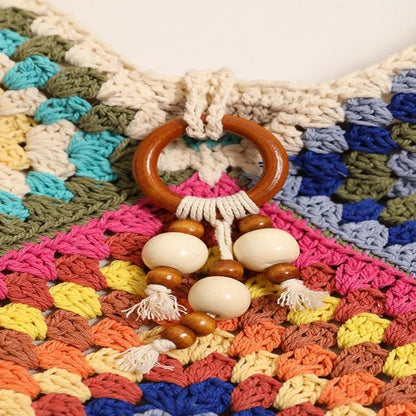 Close-up of the wooden ring and cream bead tassel detail on the colorful woven shoulder bag.