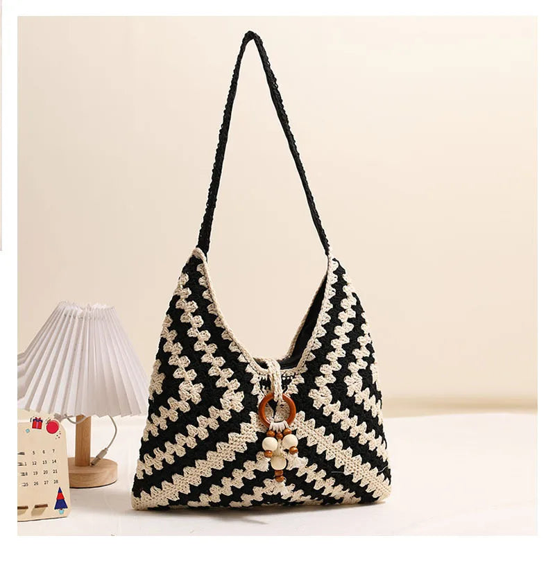 Black and cream crochet cotton shoulder bag standing upright on a beige surface beside a table lamp.