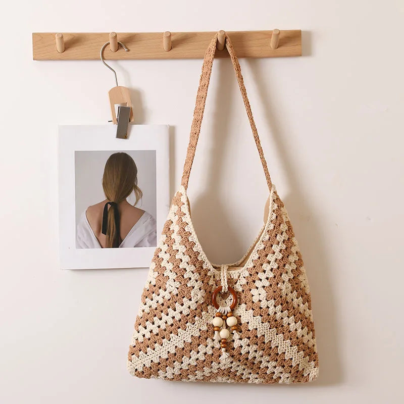 Beige and brown woven cotton shoulder bag with hanging wooden ring and bead tassels, displayed on a wooden wall hook.