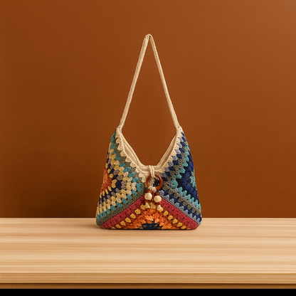 Medium cotton thread woven shoulder bag with colorful crochet pattern and long strap, placed on a wooden surface against a warm brown background.