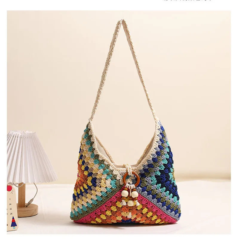 Multicolor crochet cotton shoulder bag placed on a beige background beside a small lamp and paper calendar.