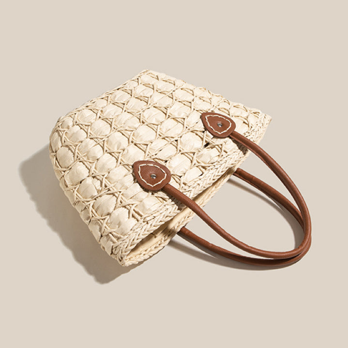 Angled view of a light straw tote bag with brown handles, showing detailed handwoven circular weave design.