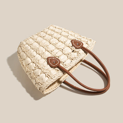 Angled view of a light straw tote bag with brown handles, showing detailed handwoven circular weave design.