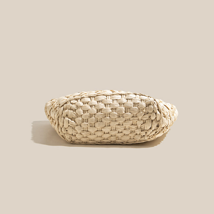Bottom view of a handwoven straw tote bag showing detailed circular weaving structure and natural straw texture.