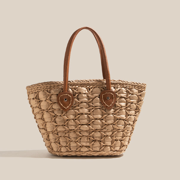 Brown-toned handwoven straw tote bag with circular weave texture and brown leather handles on a neutral beige background.