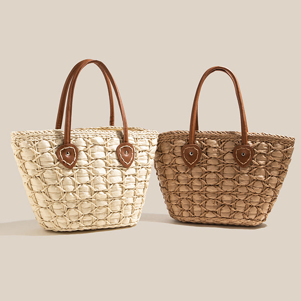 Pair of woven straw tote bags in light and dark tones, both featuring brown leather handles and circular weave patterns.