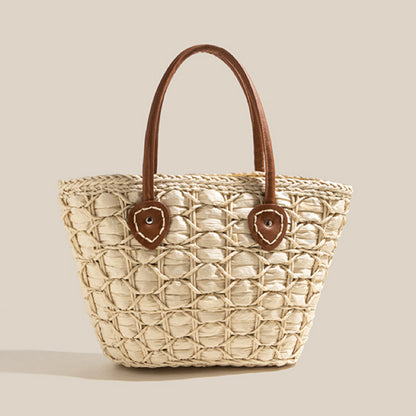 Light beige handwoven straw tote bag with circular weave and brown leather handles shown upright on a plain background.