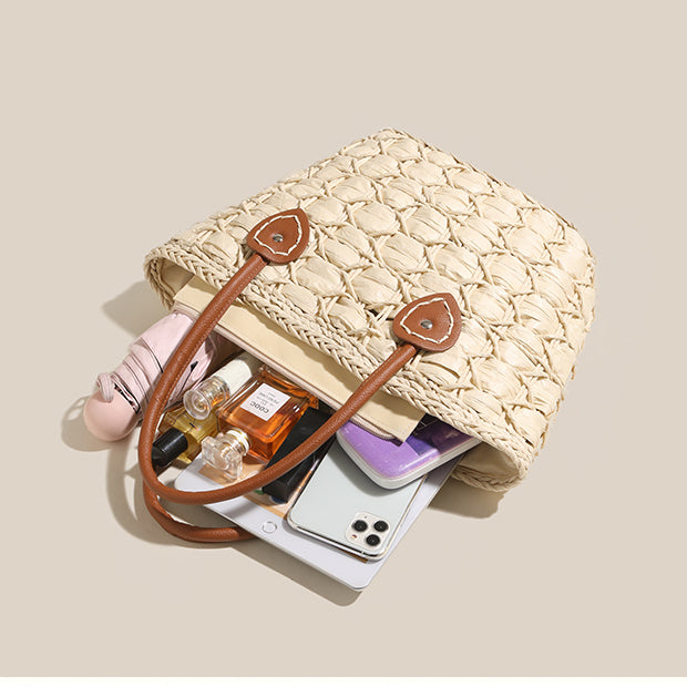 Open straw tote bag filled with everyday items such as perfume bottles, phone, and wallet, showing its roomy capacity.