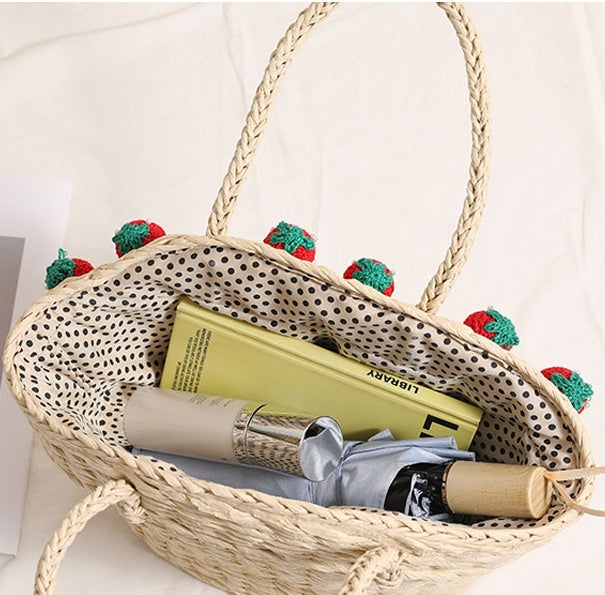 Top view of light straw beach tote bag showing dotted fabric lining and daily items inside including a book and bottle.