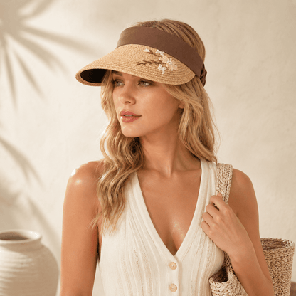 Blonde woman wearing a mocha brown floral embroidered straw visor with a cream outfit and woven tote