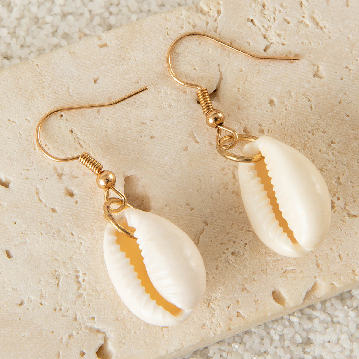 Cowrie shell earrings with polished golden hooks on natural stone surface.