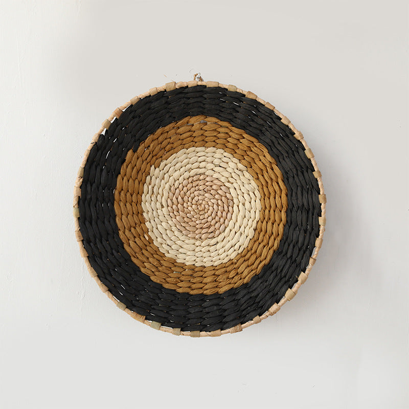 Handwoven rattan wall basket with black, tan, and cream concentric bands in natural geometric design.