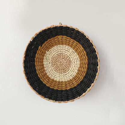 Handwoven rattan wall basket with black, tan, and cream concentric bands in natural geometric design.