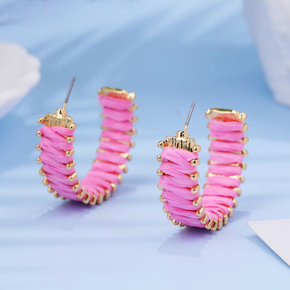 Pink handwoven straw hoop earrings with gold trim on pastel blue background.
