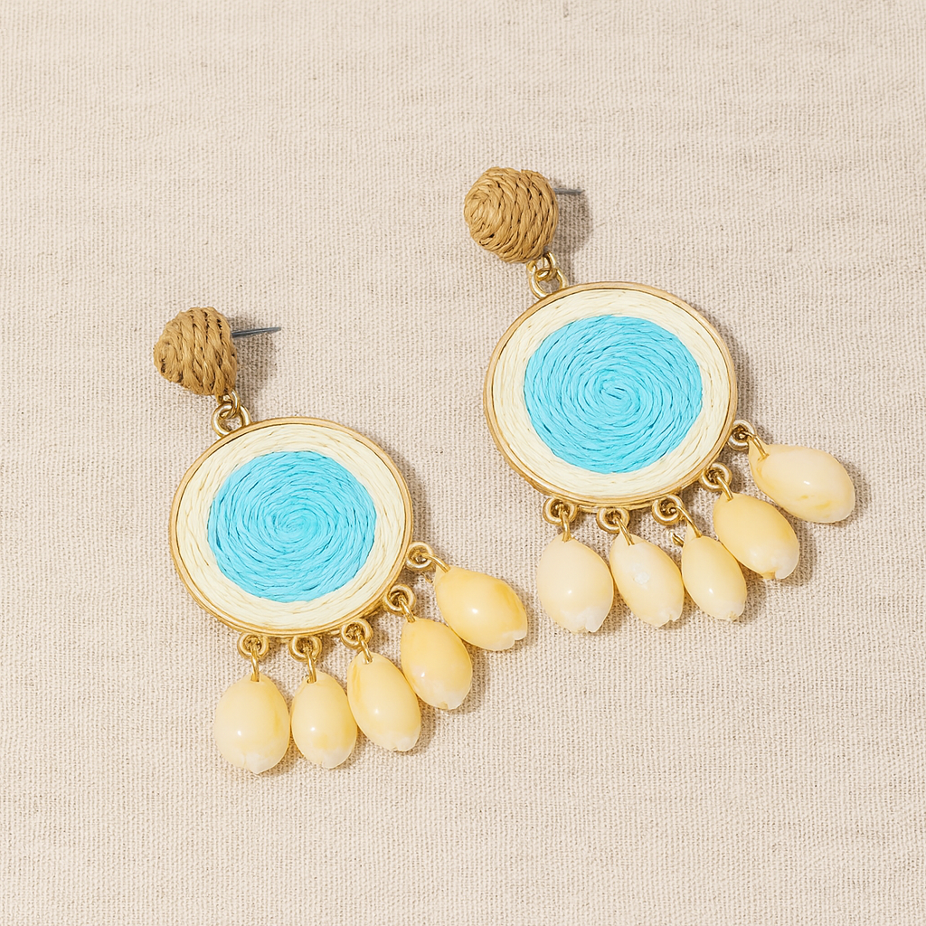 Pair of raffia-woven shell earrings in sky-blue center design displayed on linen fabric.