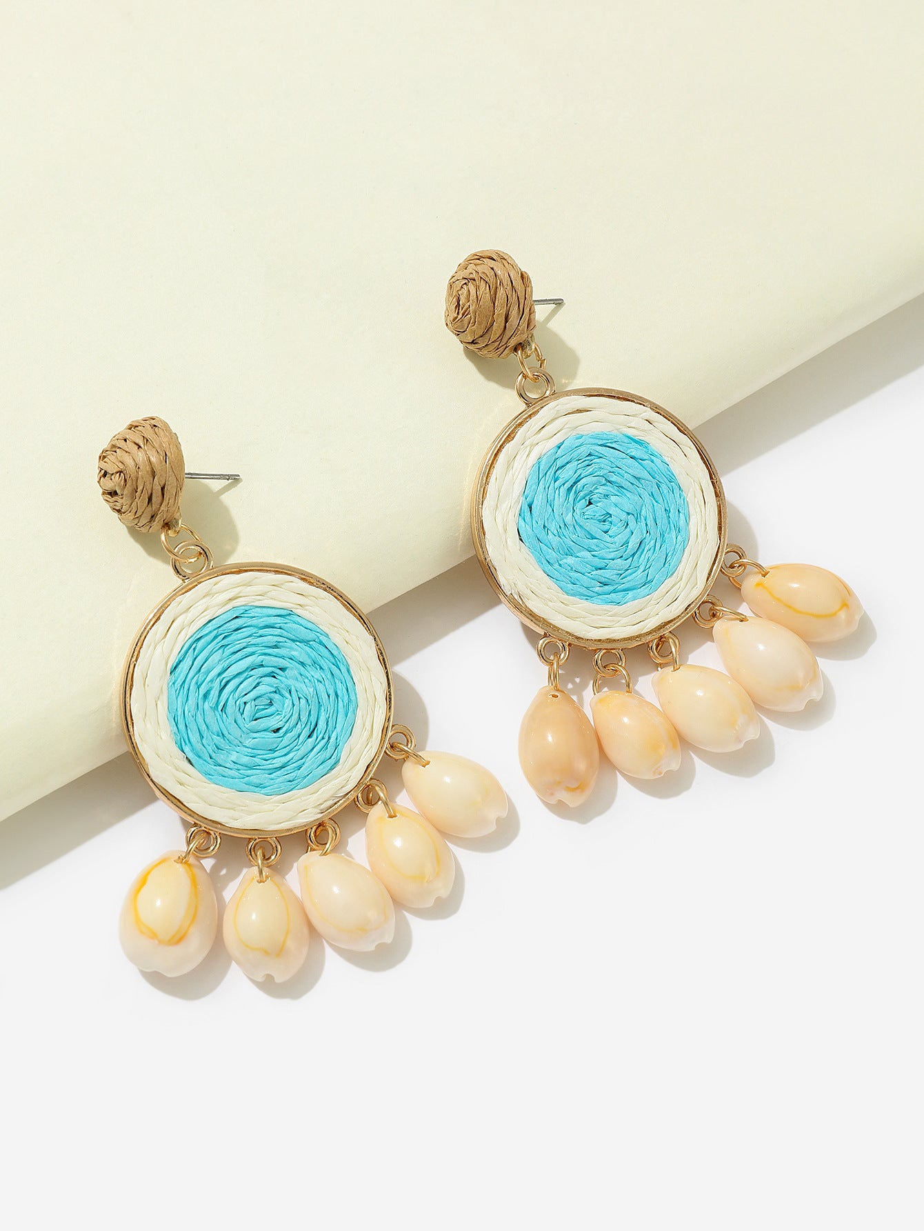 Sky-blue raffia-woven shell earrings with gold details photographed on white background.