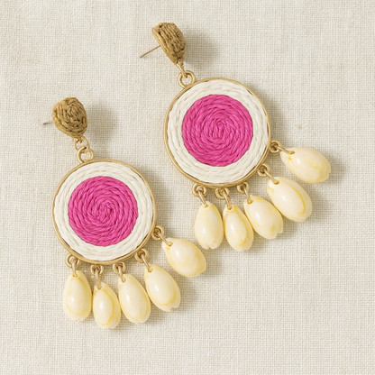 Pair of raffia-woven shell earrings in pink center design displayed on linen background.