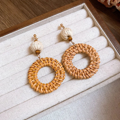 Round rattan earrings with cream fiber beads displayed in beige jewelry box.