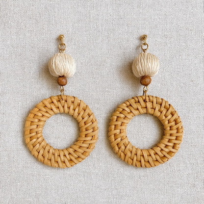 Pair of round rattan weave earrings with cream and brown beads displayed on linen fabric.