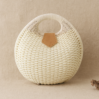 Beige round handwoven straw tote with circular handle and leather patch accent, by Solmerea.