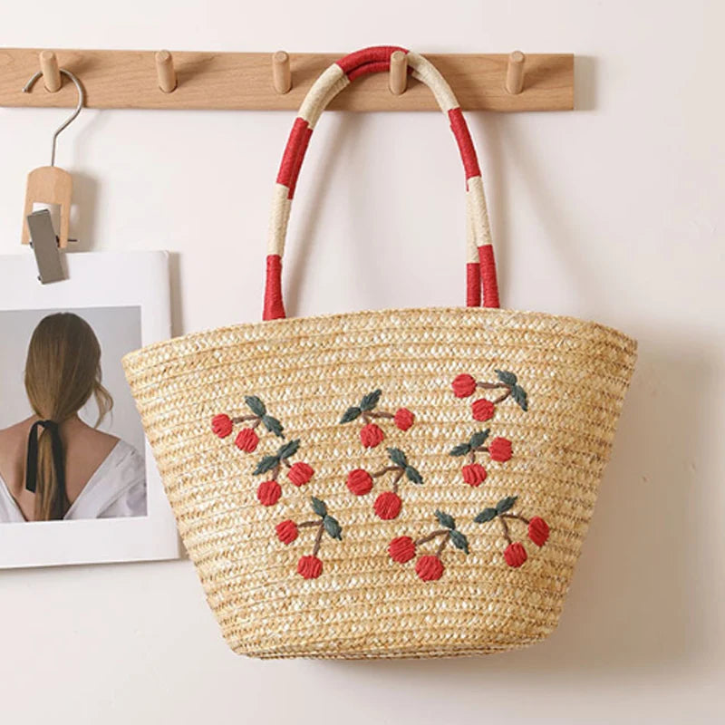 “Cherry embroidered straw tote hanging on wooden rack beside framed art, minimalist home setting, by Solmerea.”