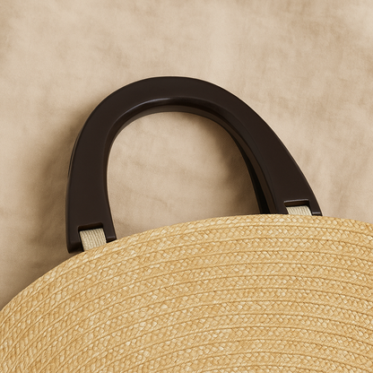 “Close-up of smooth black wooden handles attached to the woven straw clutch, showing fine craftsmanship, by Solmerea.”