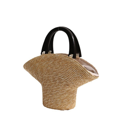 “Handwoven straw clutch photographed on light background showing unique sculptural shape and black handles, by Solmerea.”