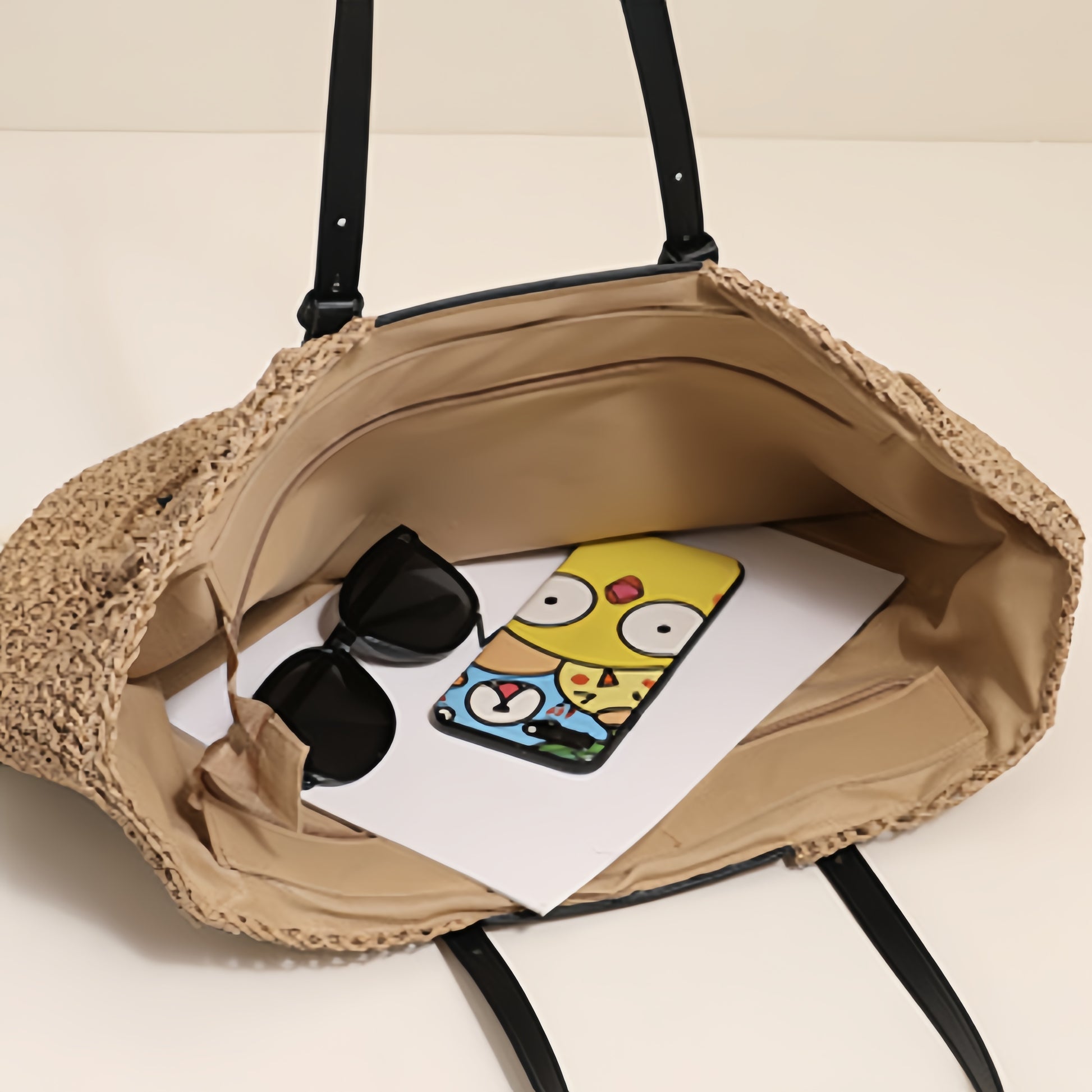 “Open straw clutch with beige lining showing phone and sunglasses inside, spacious interior, by Solmerea.”