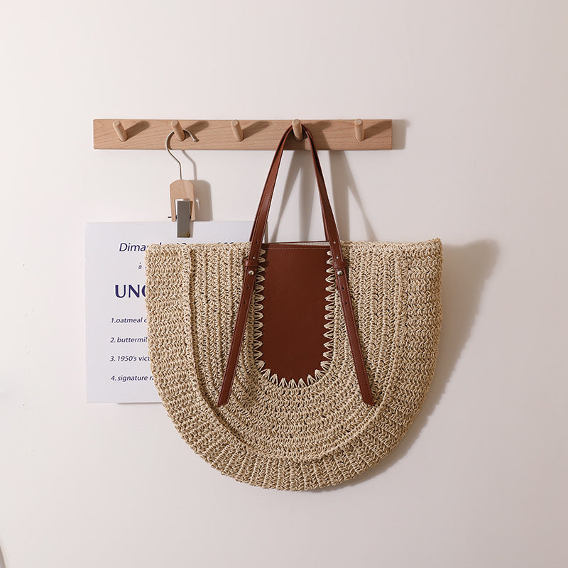 “Beige handwoven straw clutch with brown leather panel hanging on wooden rack, by Solmerea.”