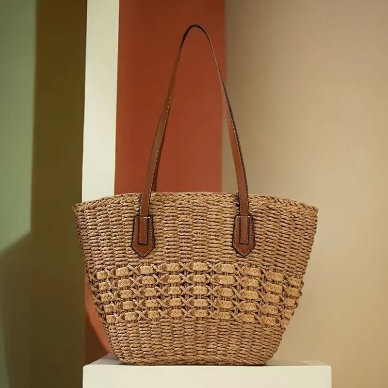 Brown woven straw shoulder bag, angled view showing tapered shape and long straps, by Solmerea.