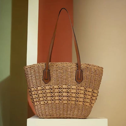 Brown woven straw shoulder bag, angled view showing tapered shape and long straps, by Solmerea.