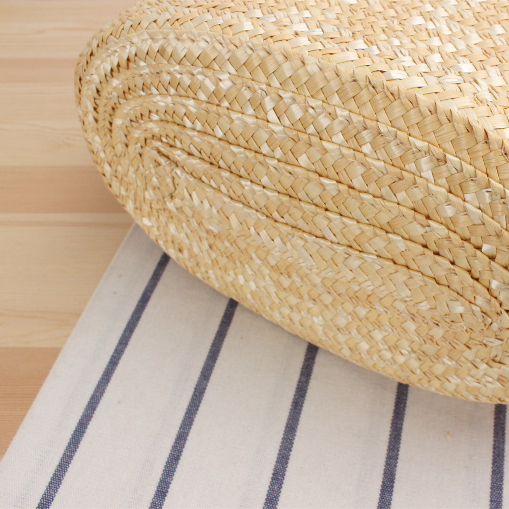 Close-up of the bottom weaving of a straw tote bag, highlighting natural raffia texture and craftsmanship.