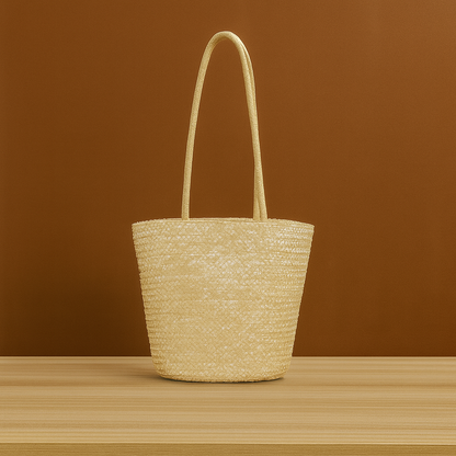 Handwoven straw beach tote bag with long handles, displayed on a wooden surface against a warm brown background.