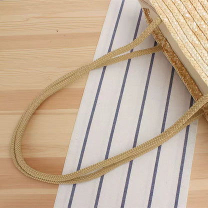 Handwoven straw beach tote bag standing upright against beige linen background, showing natural texture and simple silhouette.