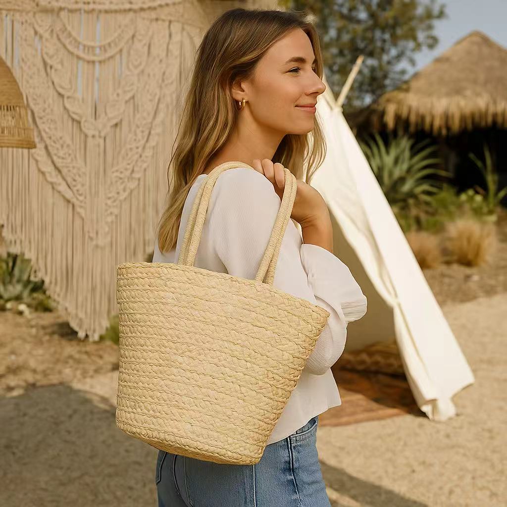Woman in casual summer outfit carrying a straw beach tote bag outdoors near a bohemian-style tent.