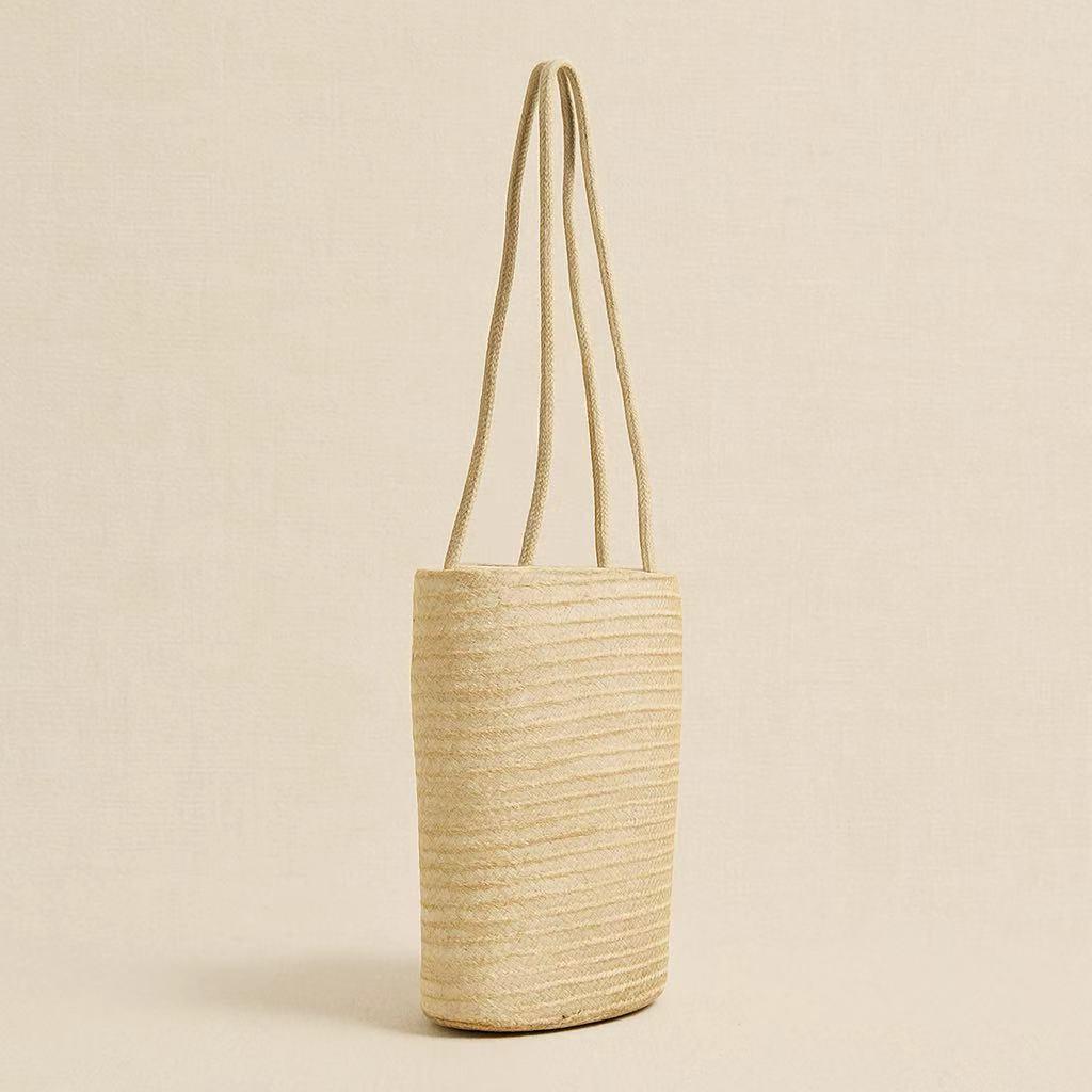 Side view of handwoven straw beach tote bag showing slim vertical structure and long shoulder straps.