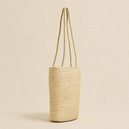 Side view of handwoven straw beach tote bag showing slim vertical structure and long shoulder straps.