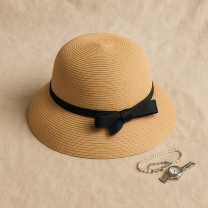 Straw hat with black ribbon bow styled beside a pearl bracelet and silver watch, showing refined feminine detail.