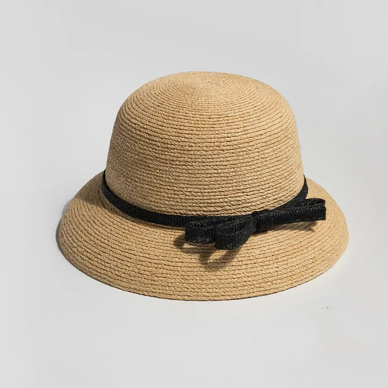 Classic straw hat with black ribbon bow, placed on bright neutral background for elegant summer styling.