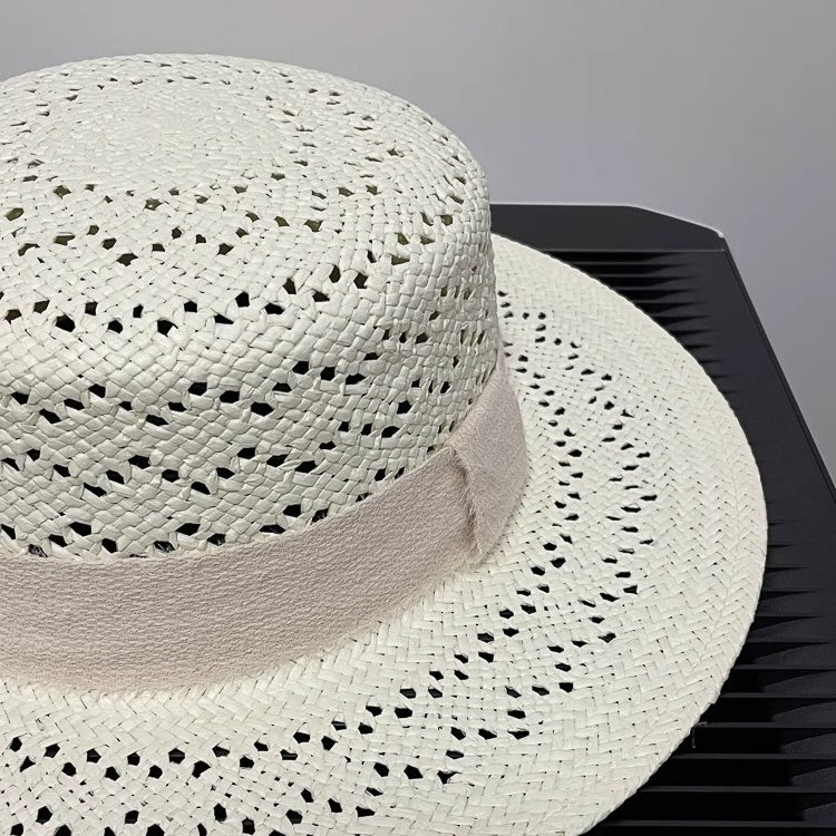 Close-up of ivory straw hat showing intricate perforated texture and fabric bow accent under neutral lighting.