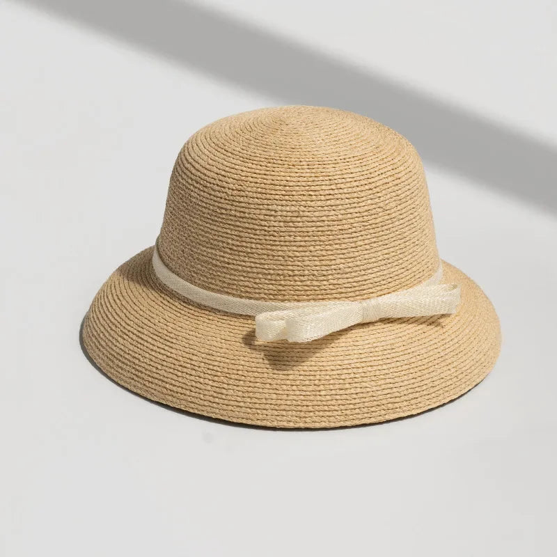 Straw sun hat with cream ribbon bow, photographed under natural sunlight on white background.