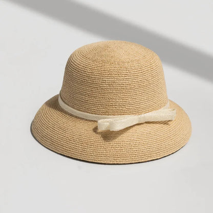 Straw sun hat with cream ribbon bow, photographed under natural sunlight on white background.