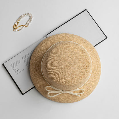 Top-down view of straw hat with cream bow, styled with pearl bracelet and open book for elegant flat-lay scene.