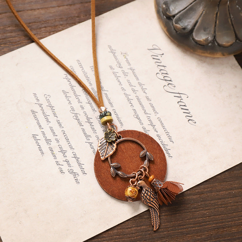 Bird motif wooden necklace with leaf and tassel decorations on natural suede cord.