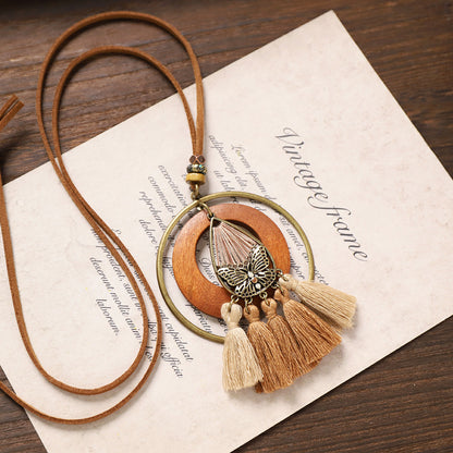 Butterfly pendant tassel wooden necklace with natural fibers and circular bronze frame on paper background.
