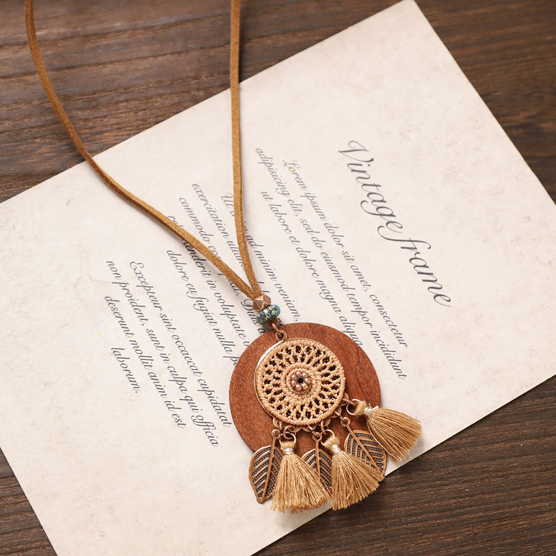 Round crochet tassel wooden necklace with bronze leaves and beige tassels displayed on rustic background.
